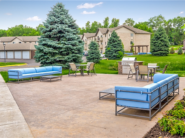 Outdoor community patio with blue-cushioned seating, tables, and a grill in a residential courtyard.