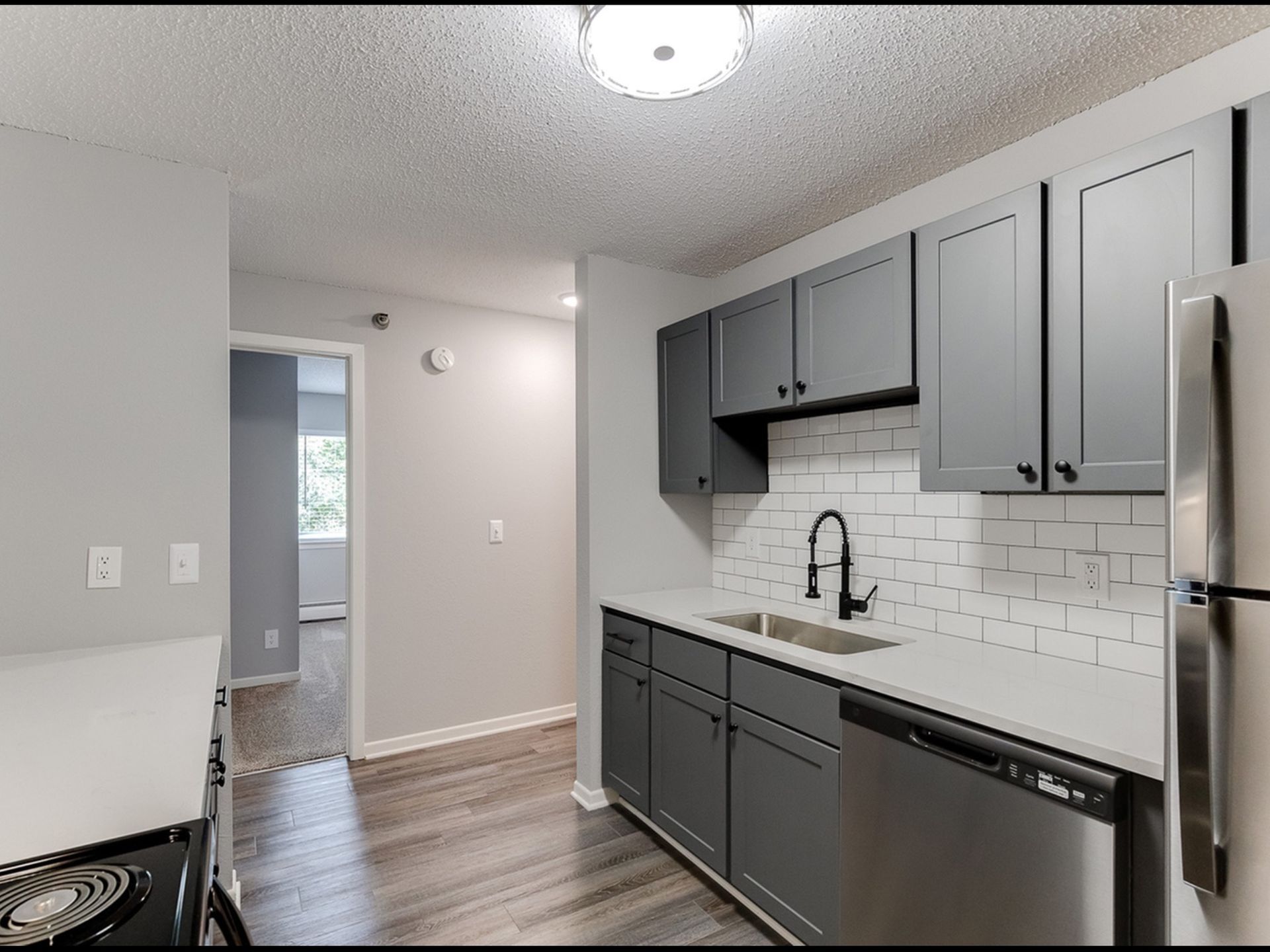 Modern apartment kitchen with gray cabinets, white subway tile backsplash and stainless steel appliances.