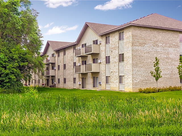 Exterior view of a brick apartment building complex with balconies and green lawn.