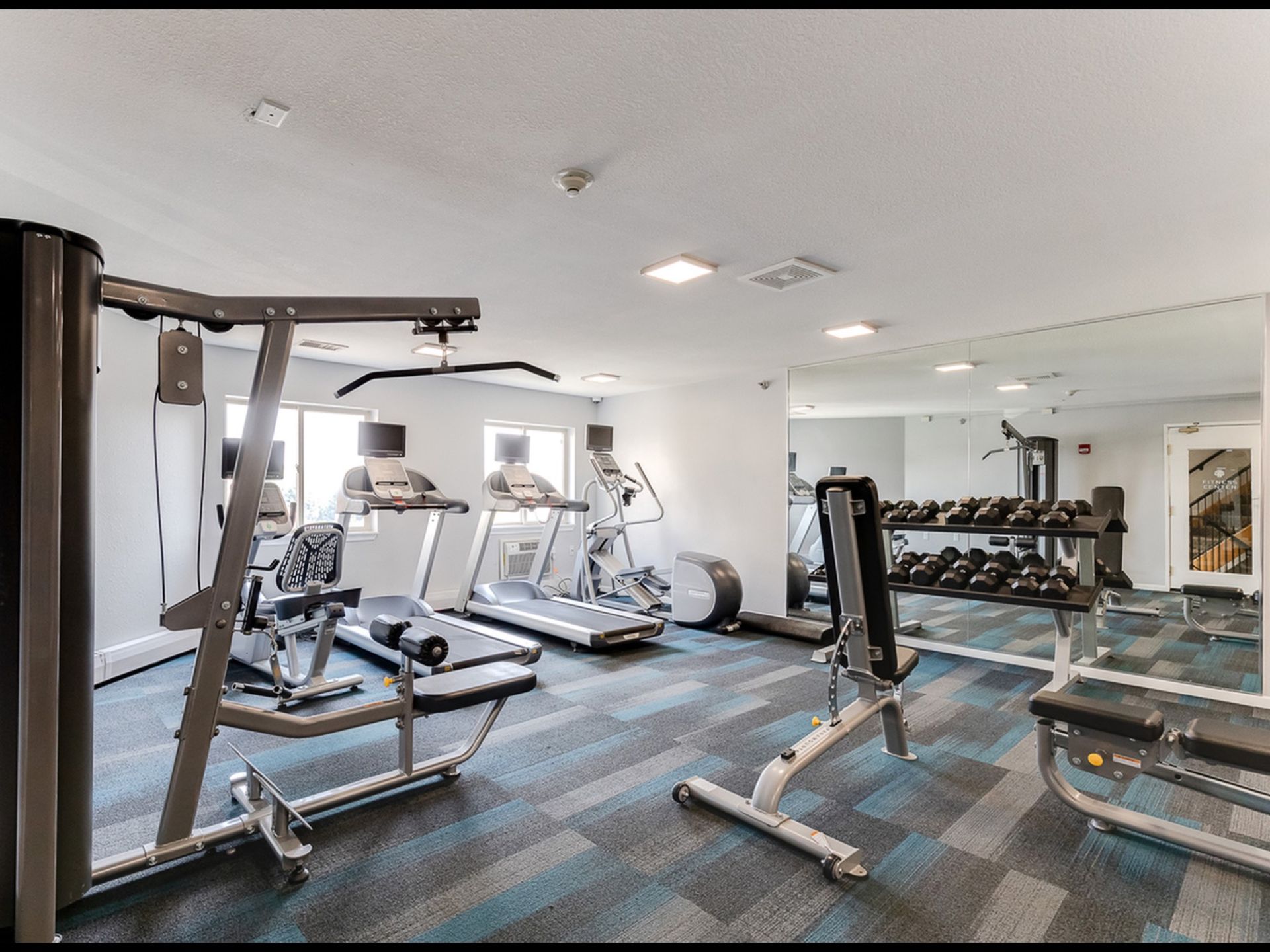 Indoor community gym with treadmills, weight machines, and a mirrored wall.
