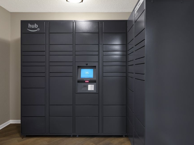 Tall dark parcel lockers with a central touchscreen in a hallway.