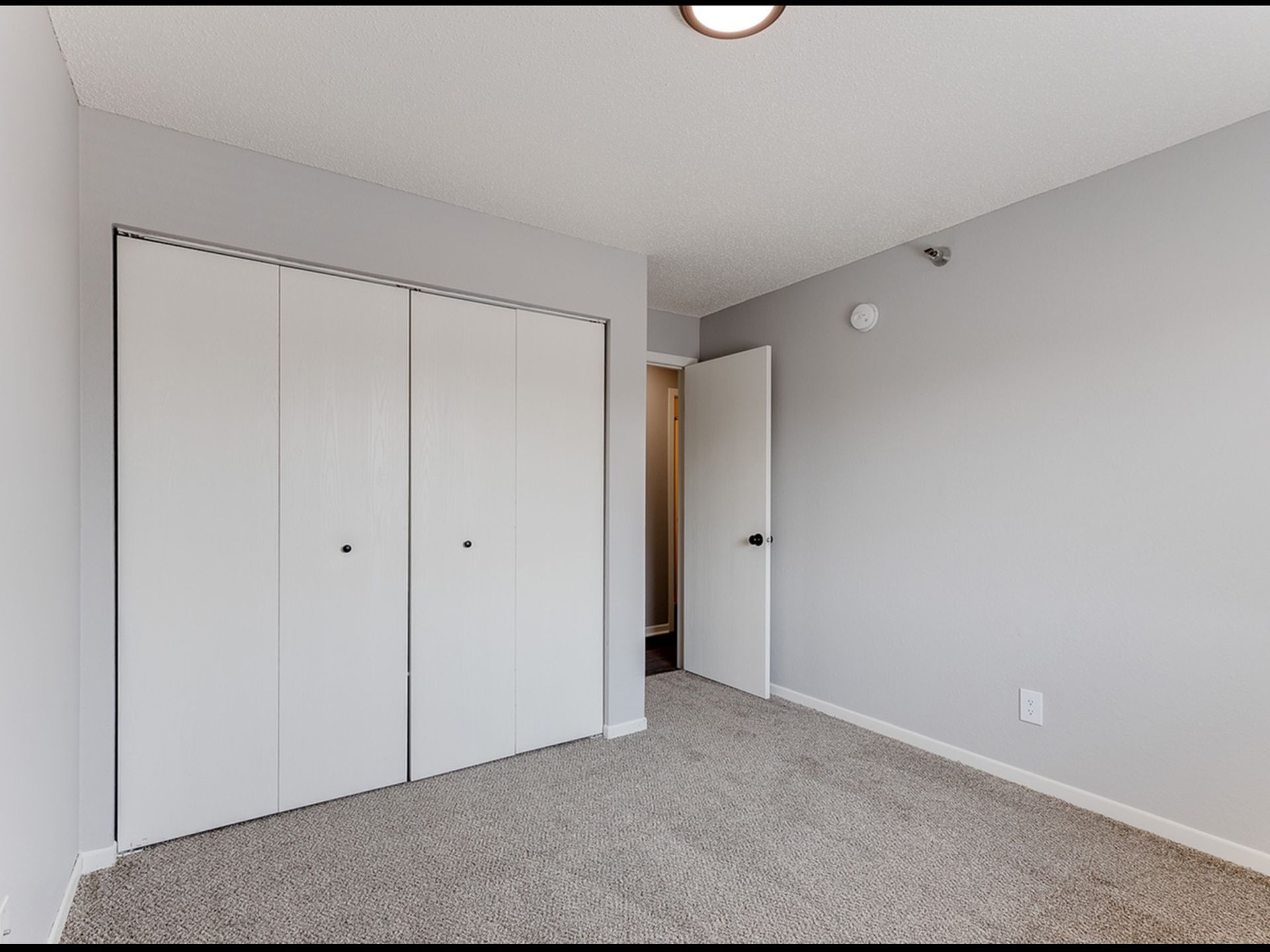 Bedroom interior with beige carpet, light gray walls, white double closet doors, and an open entry door.