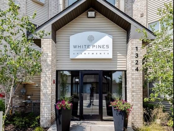 Entrance to White Pines Apartments with glass doors, a sign reading White Pines Apartments, and two flower planters.