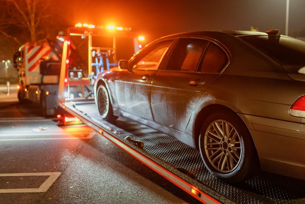 A car is being towed by a tow truck at night.