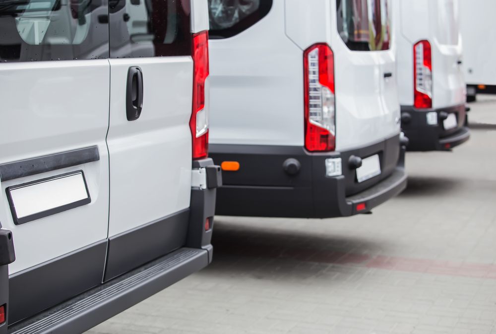 A row of white vans parked next to each other in a parking lot.
