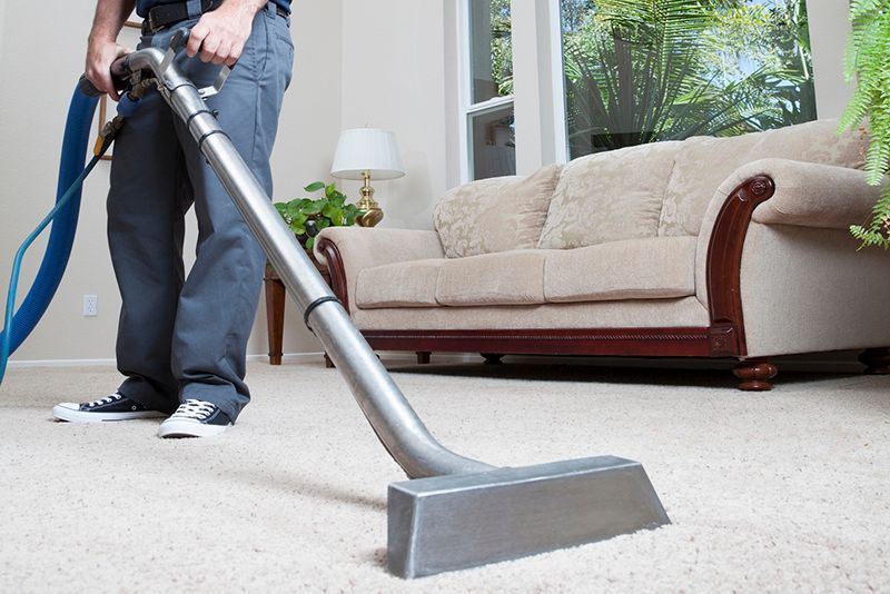 A man is using a vacuum cleaner to clean a carpet in a living room.
