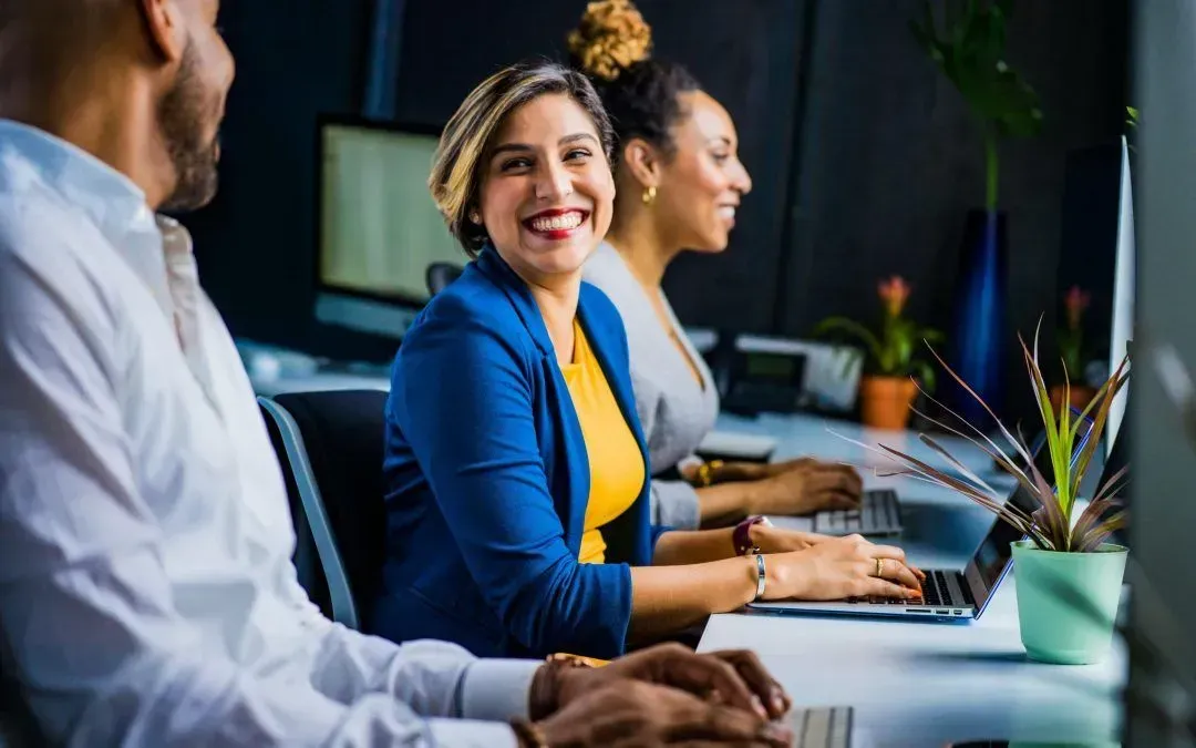 Three people smiling and working at computers in office setting