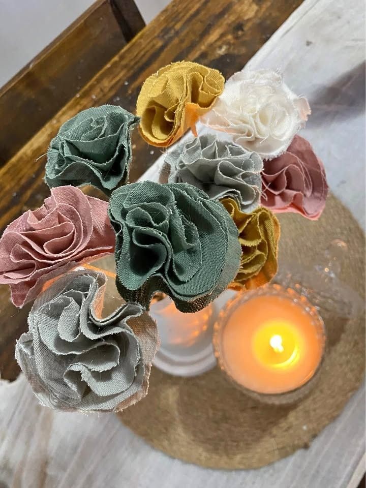 Flores de tela de colores en un jarrón con una vela encendida sobre un posavasos de piedra.