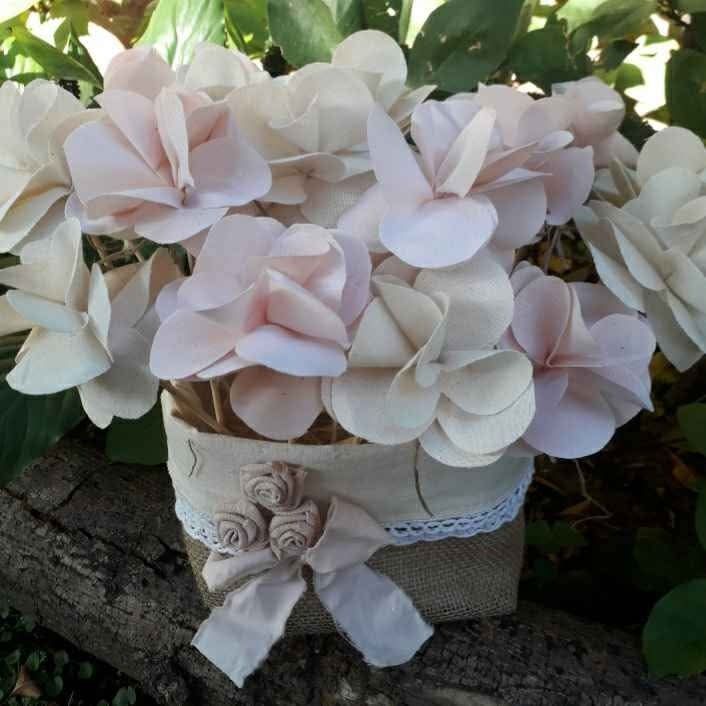 Flores de papel de color crema en una maceta de arpillera, decoradas con encaje y un lazo, colocadas sobre un tronco.