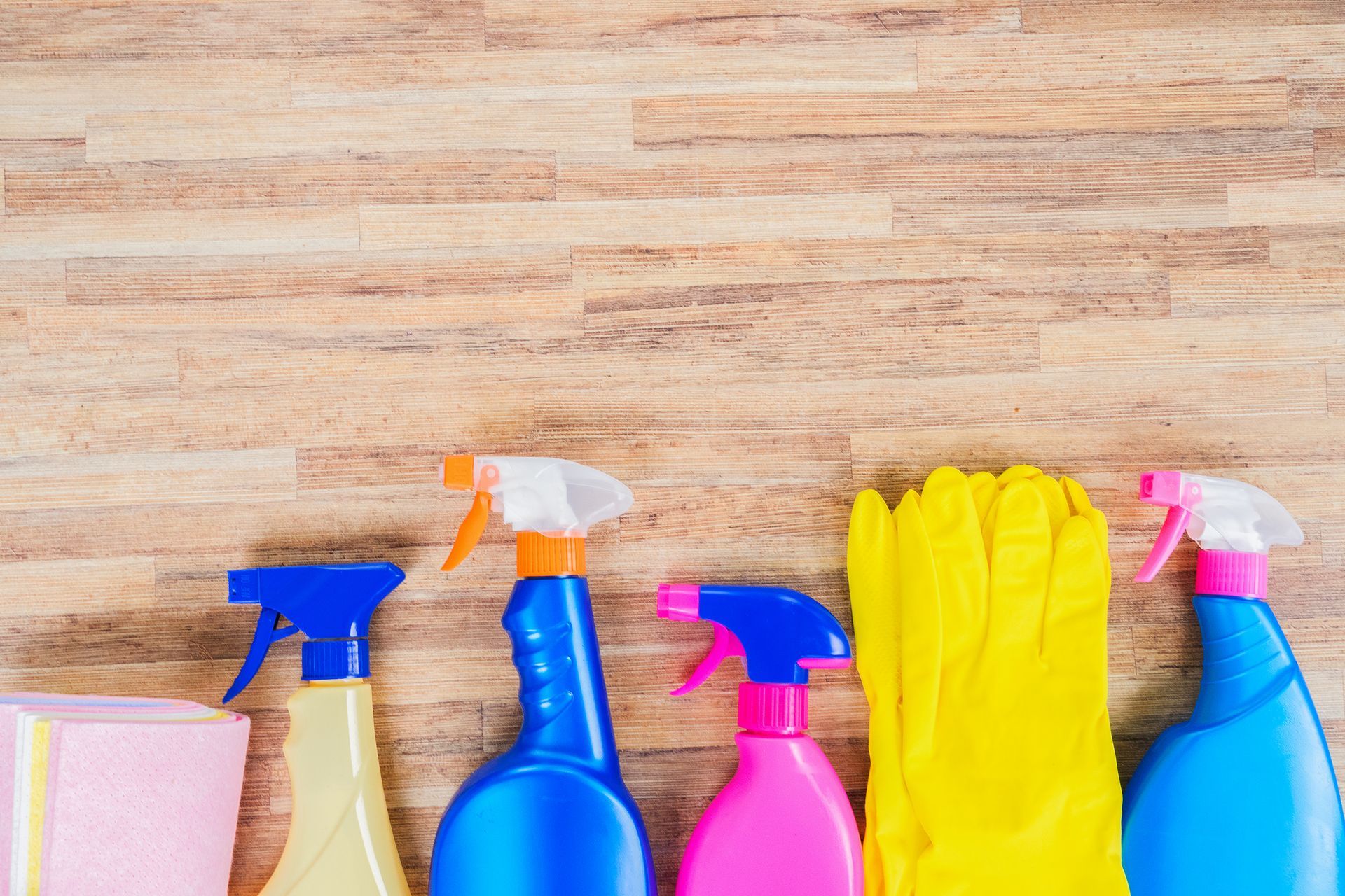 cleaners for homes A row of spray bottles , gloves , and sponges on a wooden table.