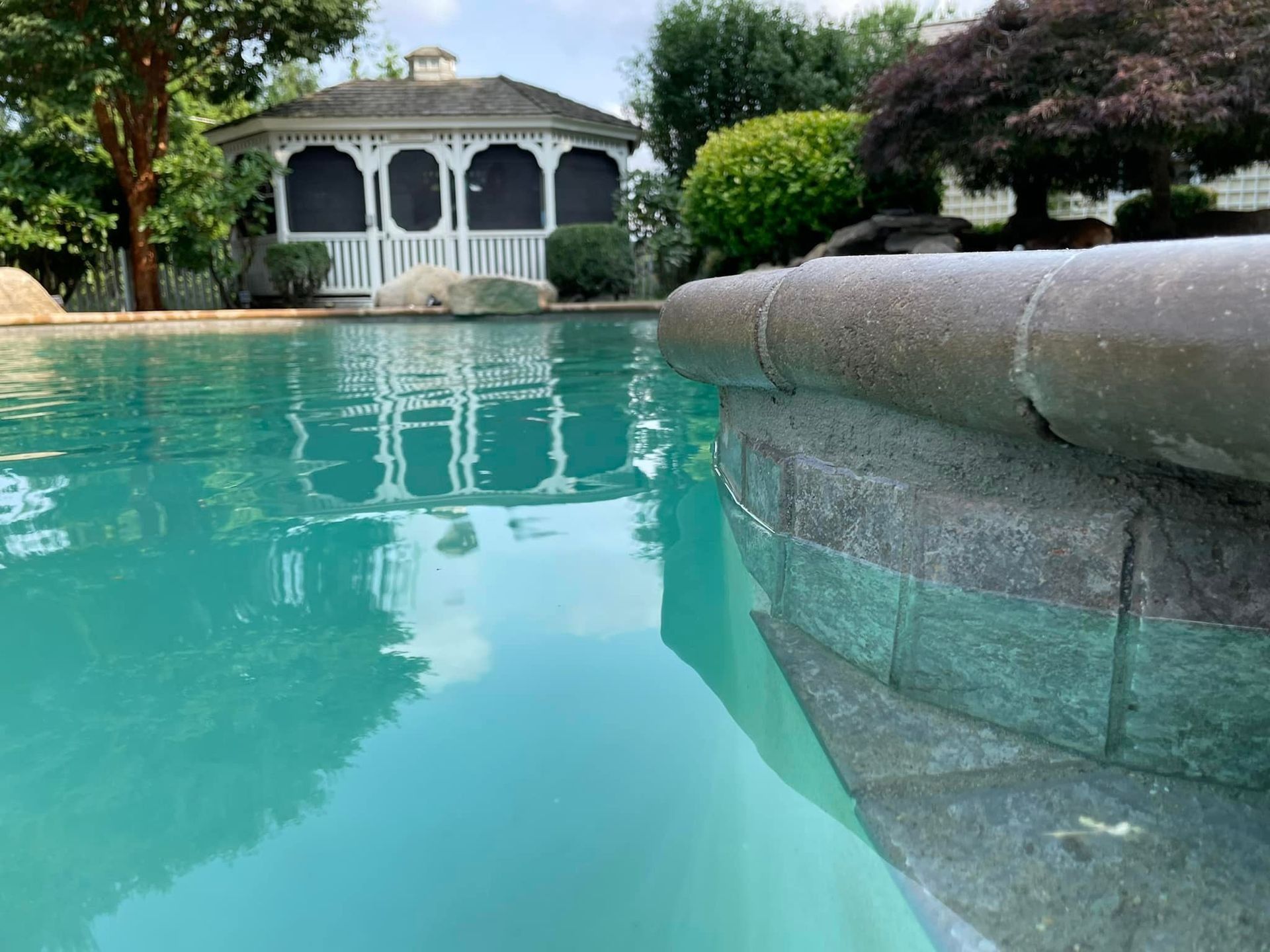 Pool water with a gazebo in the background. Stone edge in the foreground, water reflection.