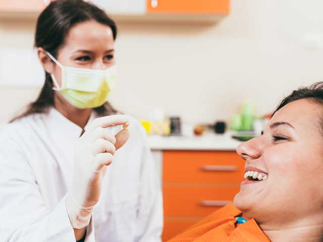 A woman is sitting in a dental chair while a dentist wearing a mask and gloves examines her teeth.