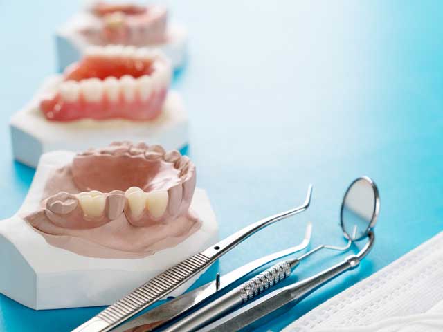 A row of dentures and dental instruments on a blue table.