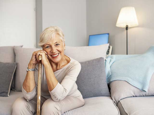 An elderly woman is sitting on a couch with a cane.