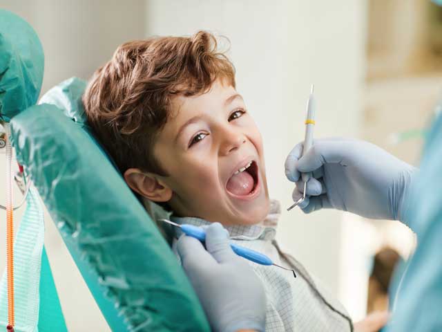 A young boy is sitting in a dental chair while a dentist examines his teeth.