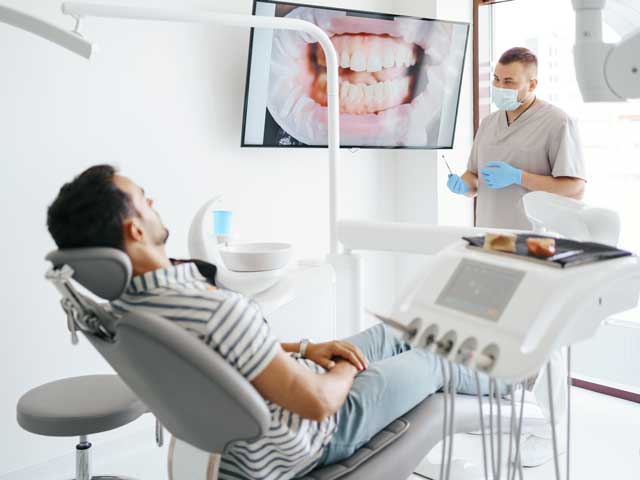 A man is sitting in a dental chair while a dentist looks at his teeth.