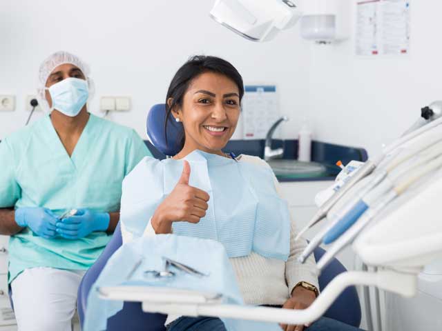 A woman is giving a thumbs up while sitting in a dental chair.