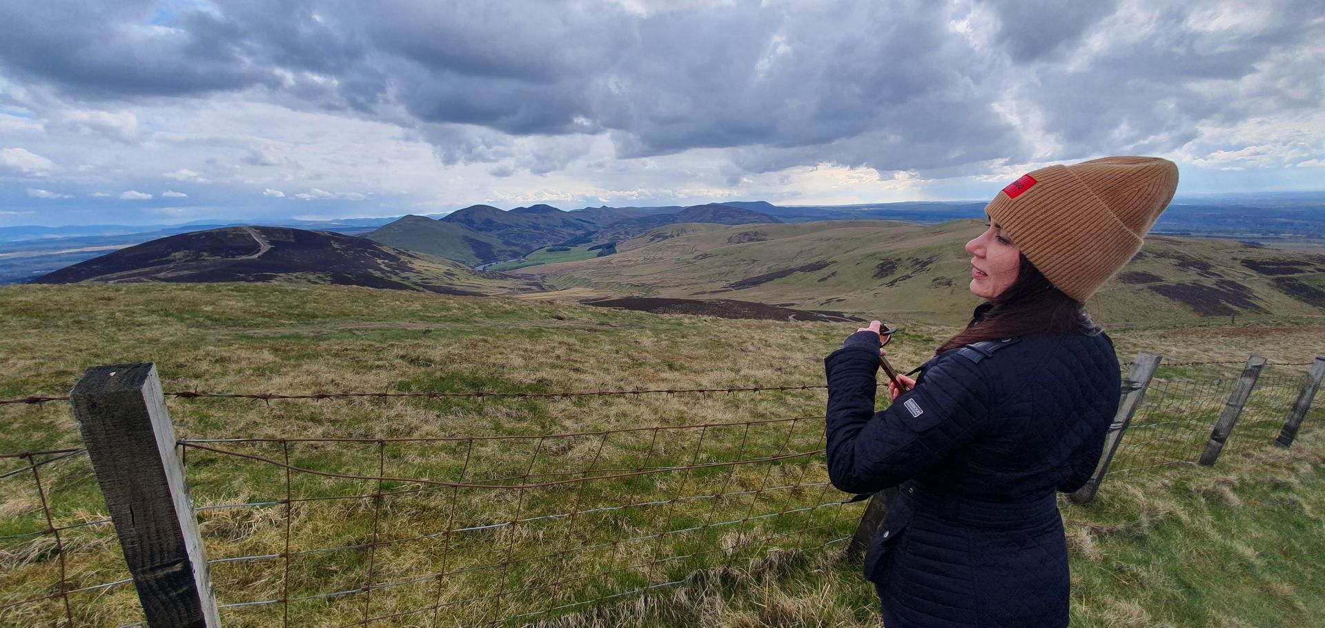 Image of a female tourist on an Edinburgh Skyline eco-tour looking southwest over the main group of hills in the Pentland Regional Park. Eco-tour provided by Tartan Compass Tours.