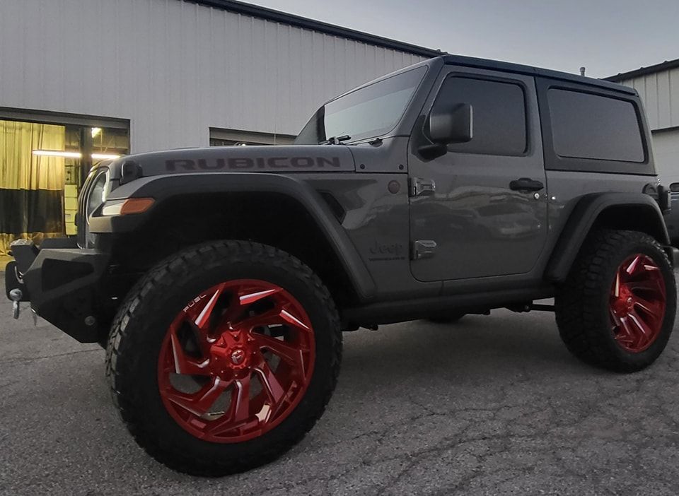 A jeep wrangler with red wheels is parked in front of a building.