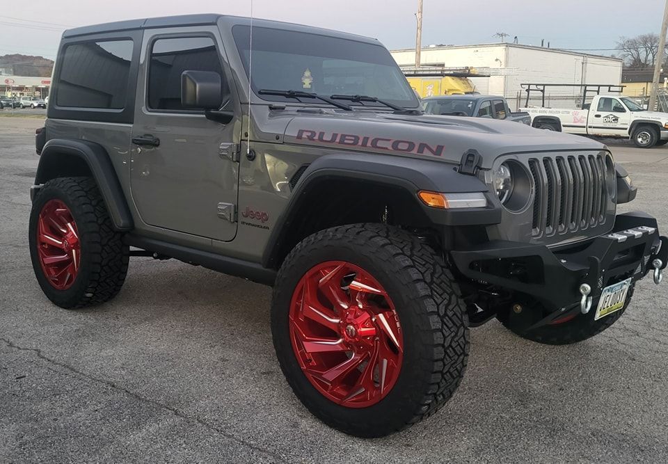 A jeep wrangler with red wheels is parked in a parking lot.