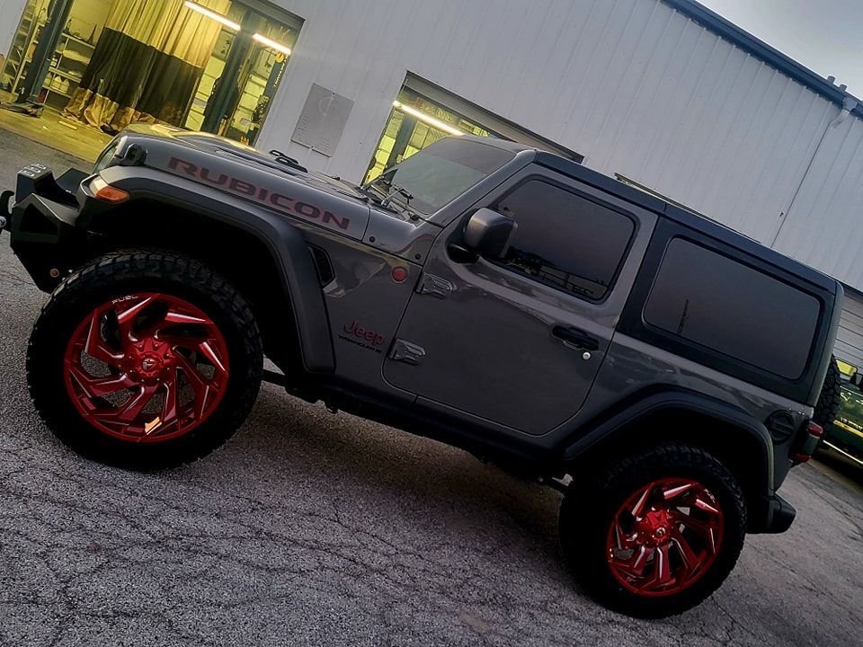 A jeep wrangler with red wheels is parked in front of a building.