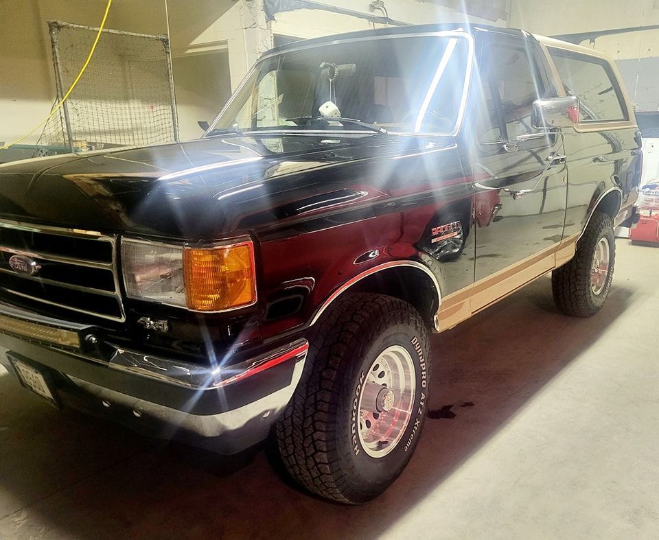 A red and black ford bronco is parked in a garage.