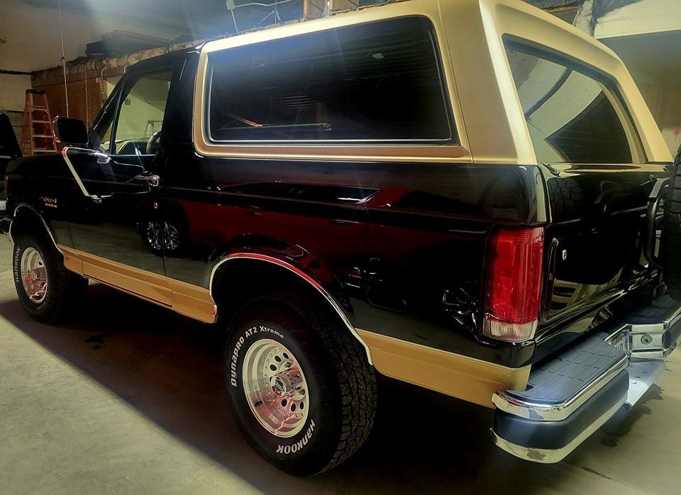 A black and gold ford bronco is parked in a garage.