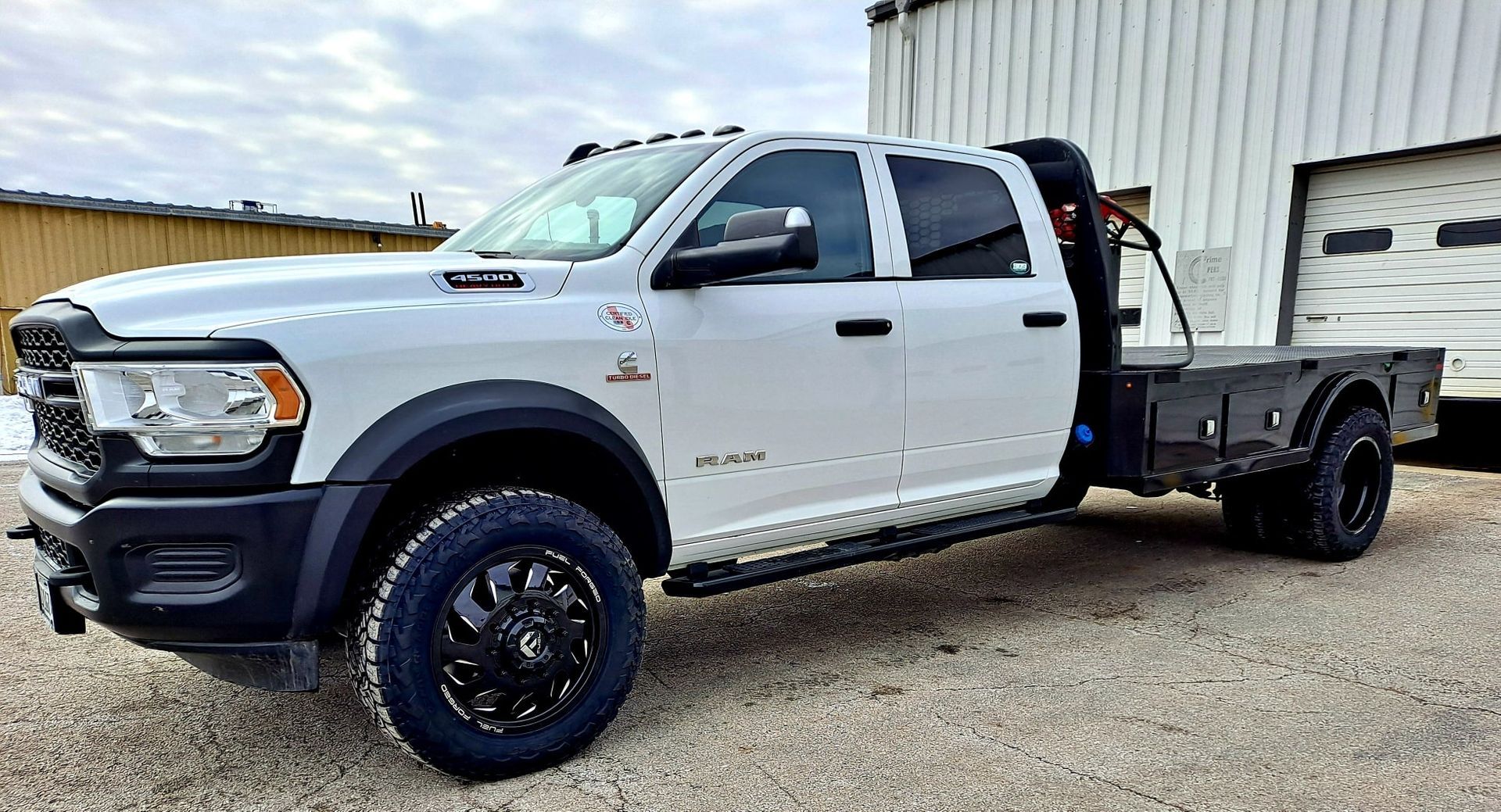 A white ram truck with a flat bed is parked in front of a building.