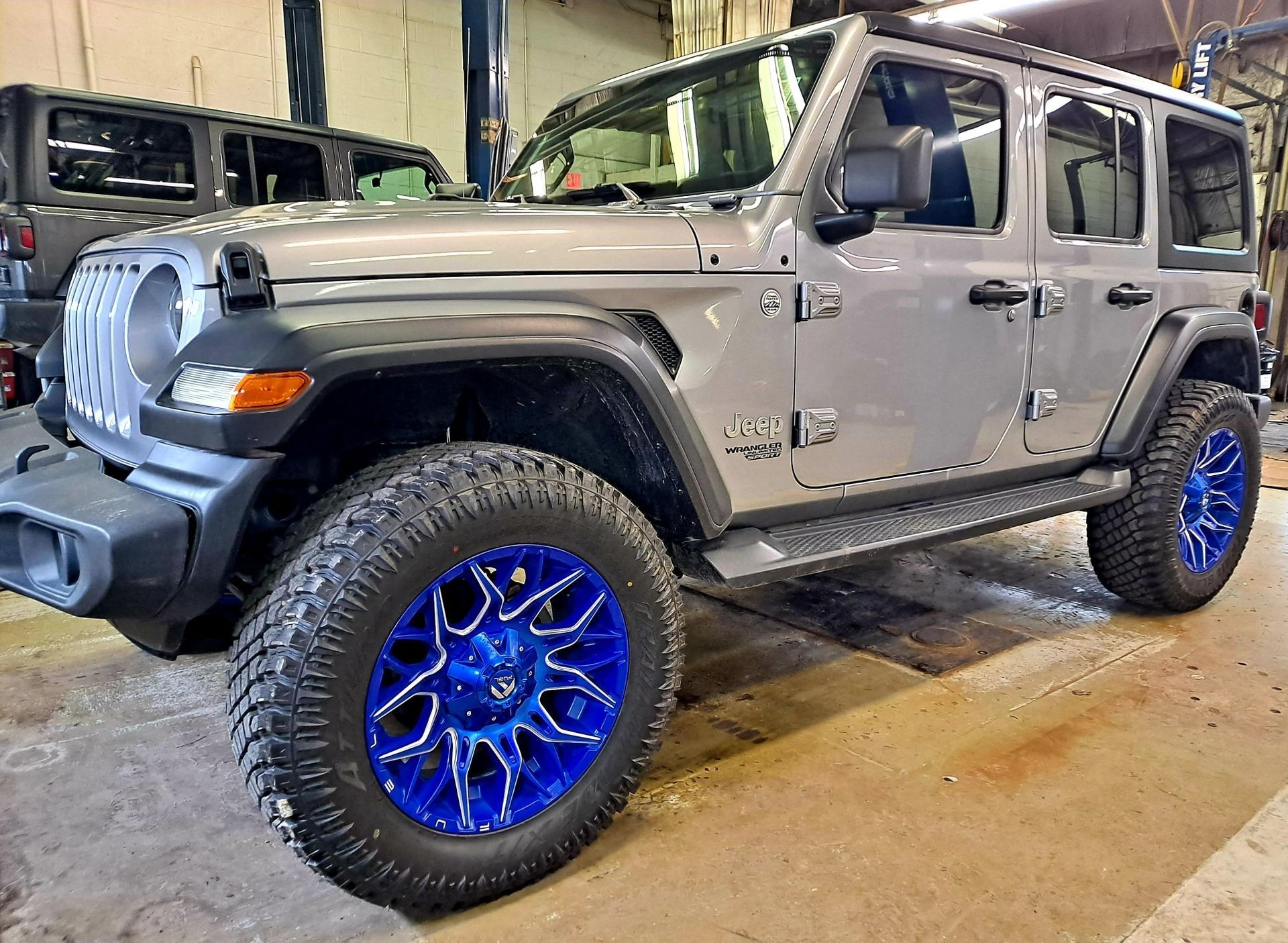 A silver jeep with blue wheels is parked in a garage.