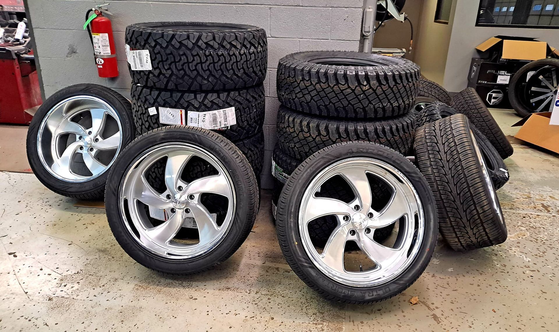 A bunch of tires and wheels are stacked on top of each other in a garage.