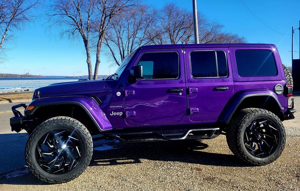 A purple jeep is parked on a gravel road next to a body of water.