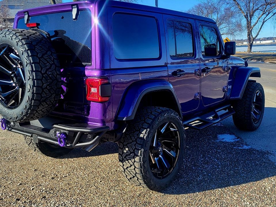 A purple jeep wrangler is parked on a gravel road.