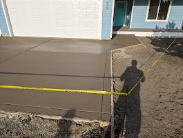 A man is measuring a concrete driveway in front of a house.