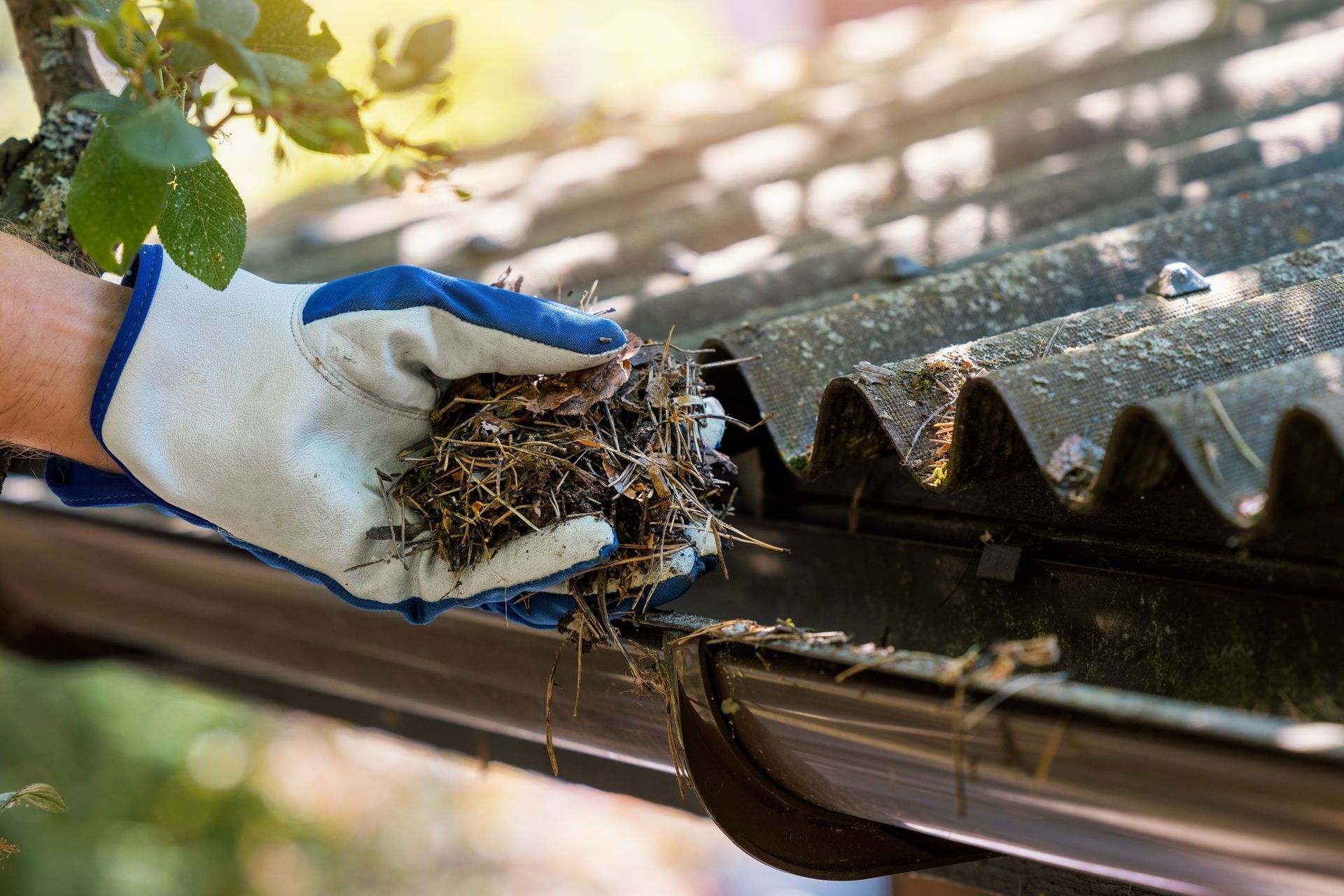 A person wearing gloves is cleaning a gutter on a roof.