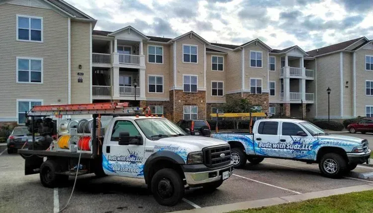 Two trucks are parked in front of a large apartment building.