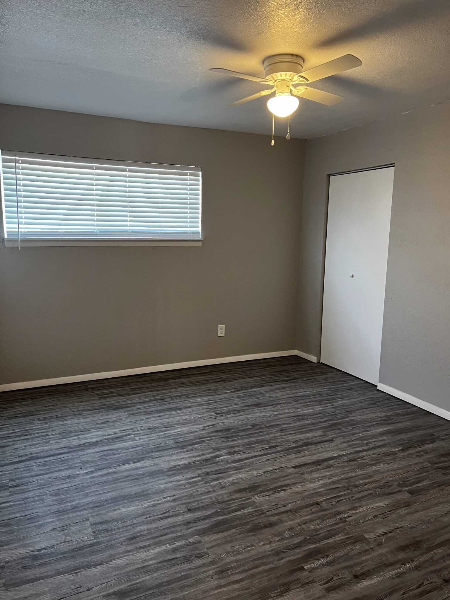 Empty room with dark gray floor, gray walls, closed white door, and window with blinds.