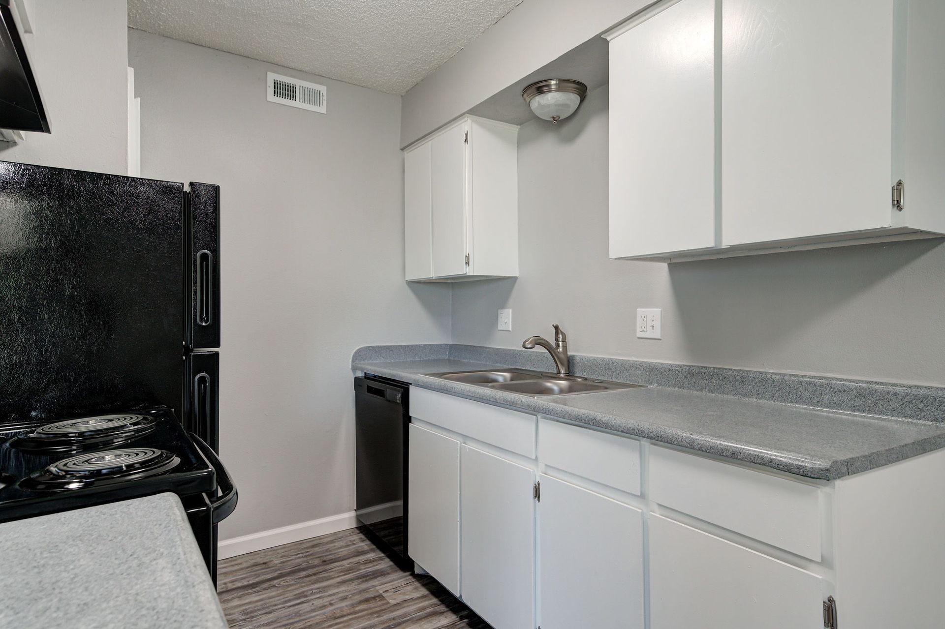 Kitchen with white cabinets, gray countertops and walls, and black appliances.