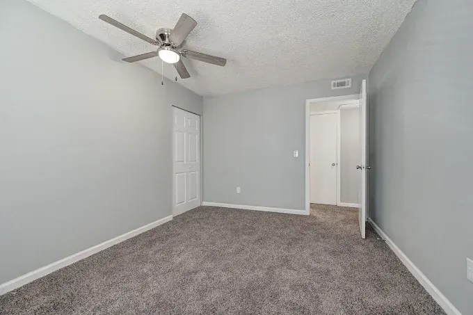 Empty bedroom with gray walls, carpet, ceiling fan, and open door to hallway.