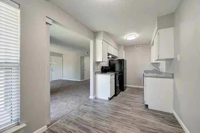 Kitchen with white cabinets, gray countertops, and wood-look flooring, leading to a room with carpet.