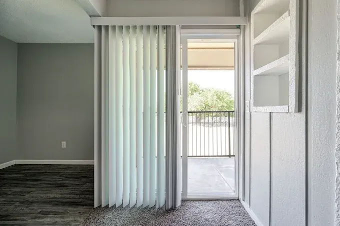 Room with open door to a balcony. Vertical blinds, gray walls, and built-in white shelving.