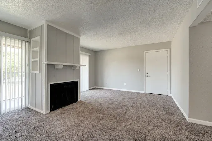 Empty living room with gray walls, carpet, fireplace, and sliding door to a balcony.