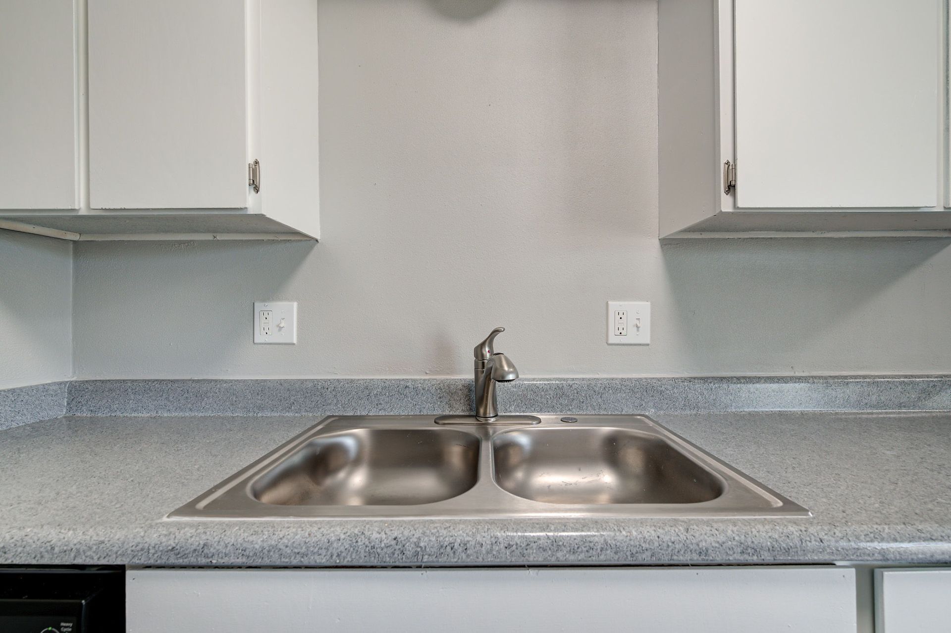 Stainless steel kitchen sink with cabinets and speckled countertop.