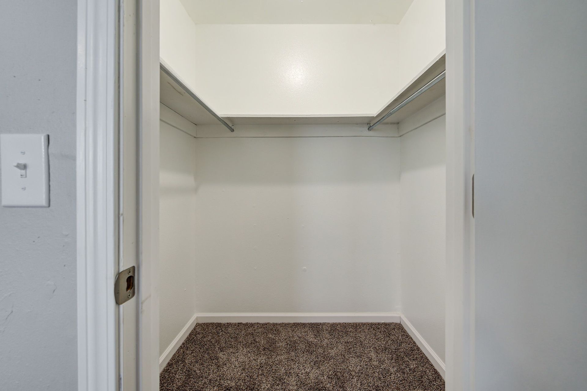 Empty white-walled closet with upper shelves and a carpeted floor. Door is open.