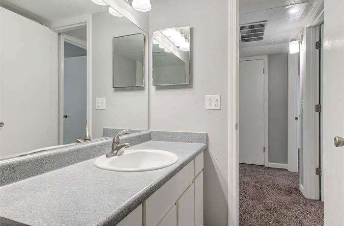Bathroom with a white sink, grey countertop, large mirror, and open doorway to a hallway.