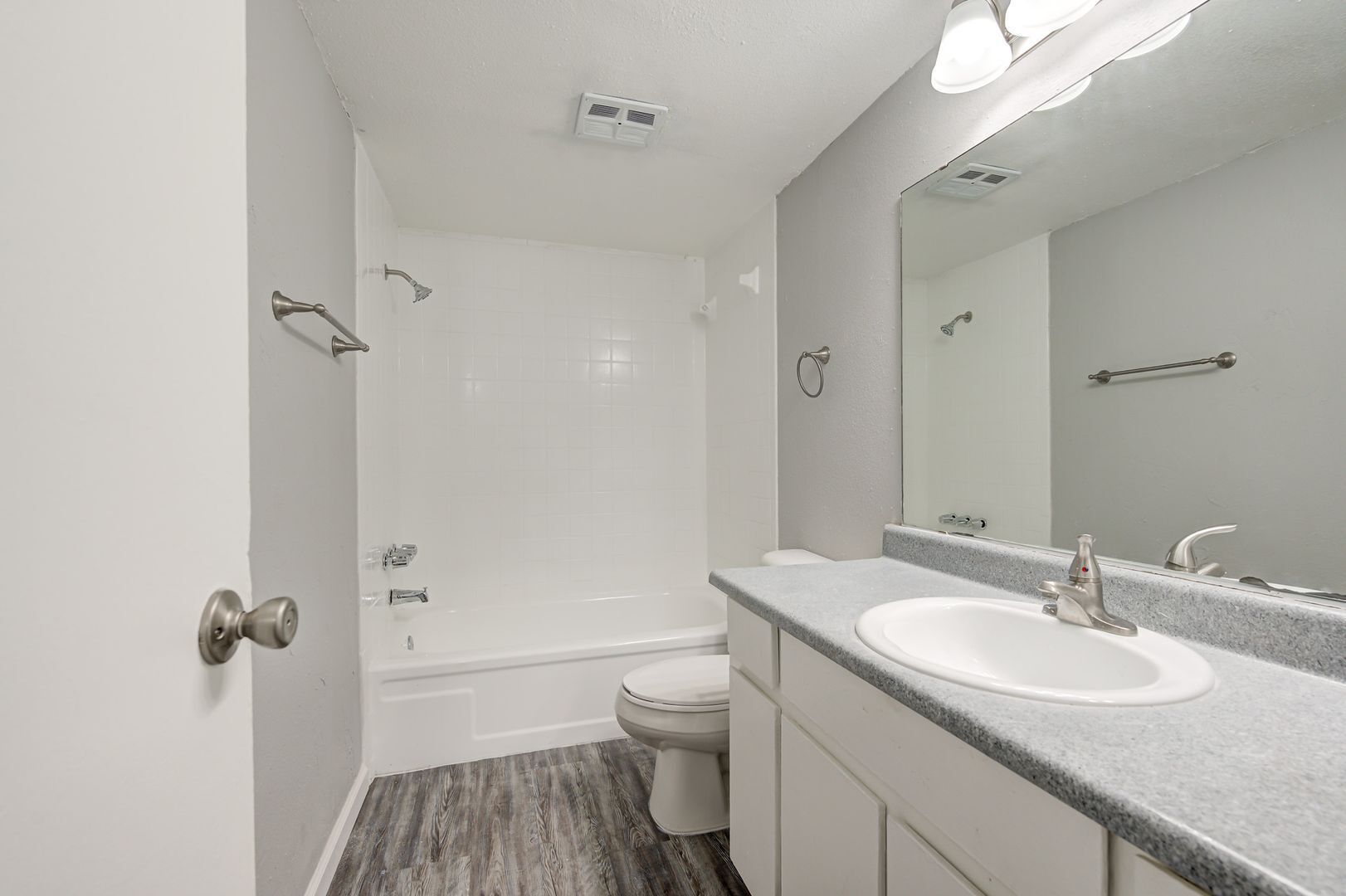 Bathroom with white fixtures, gray walls, and wood-look flooring. Sink, toilet, and bathtub visible.
