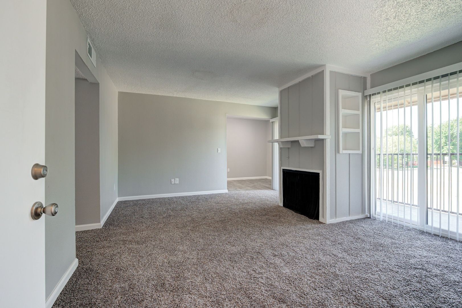 Empty living room with gray walls, carpet, fireplace, and sliding door to balcony.