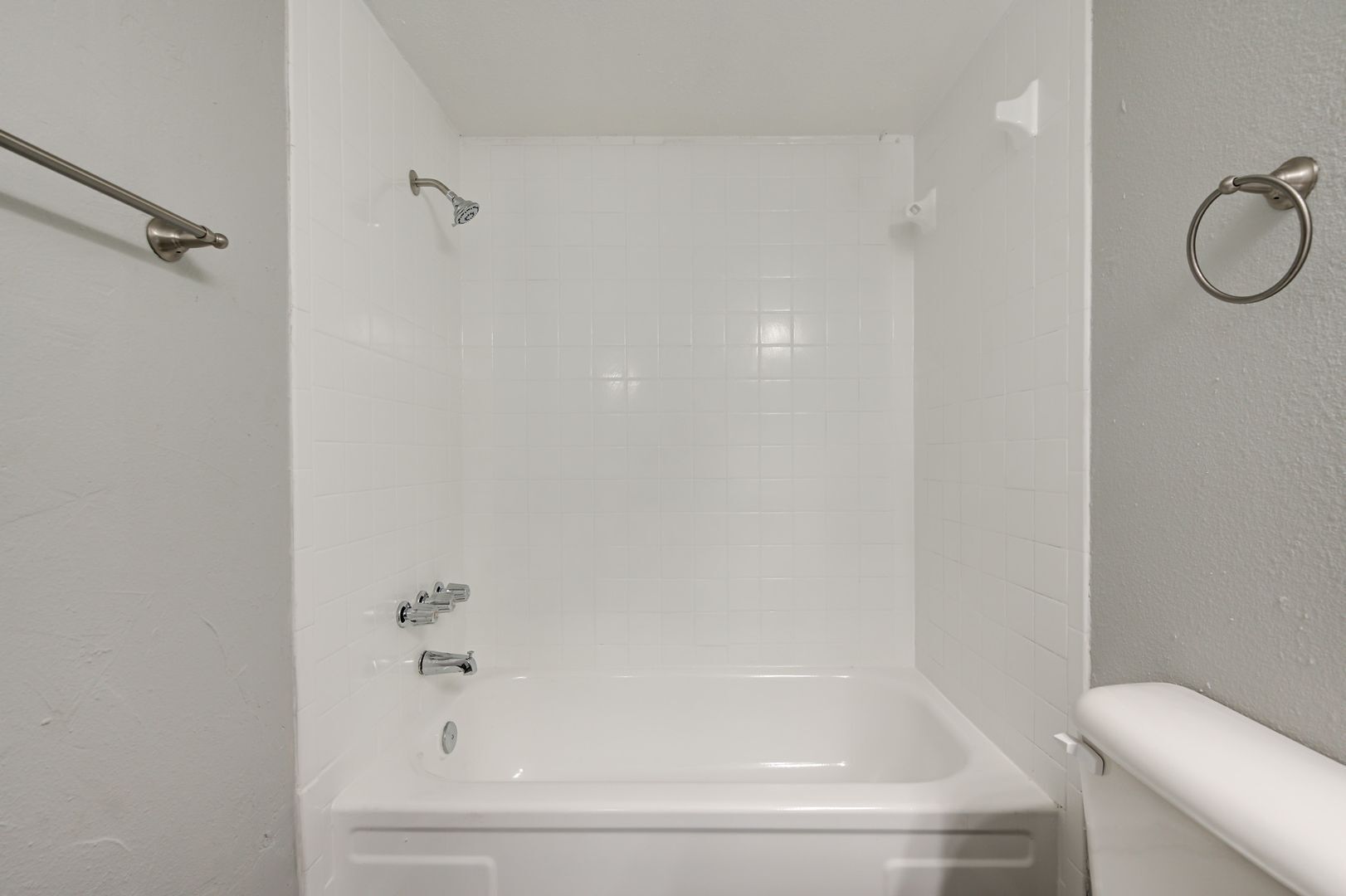 White bathroom with bathtub and shower, light gray walls, towel rack, toilet.