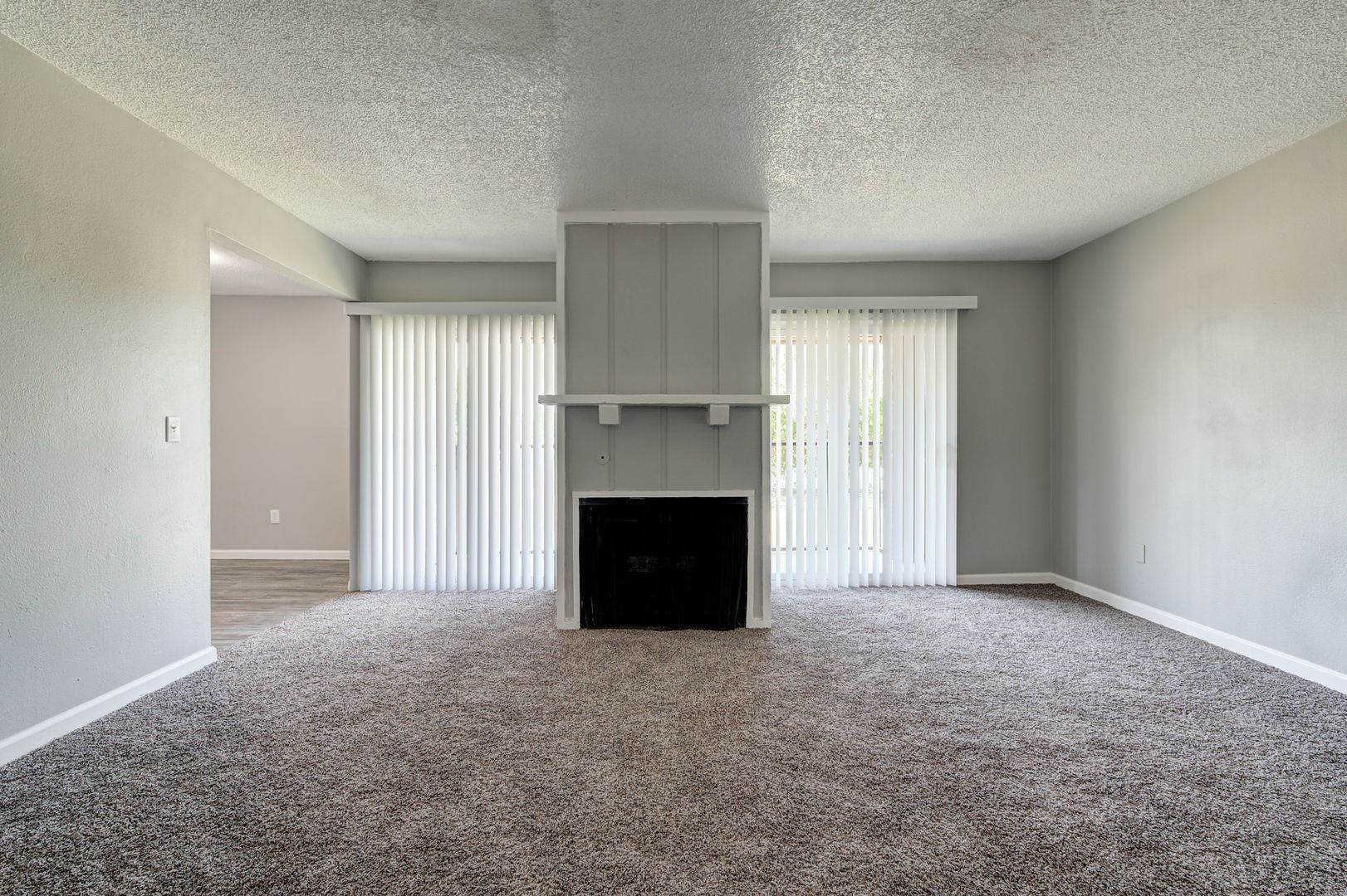 Living room with gray walls, carpet, fireplace, and sliding glass doors with vertical blinds.