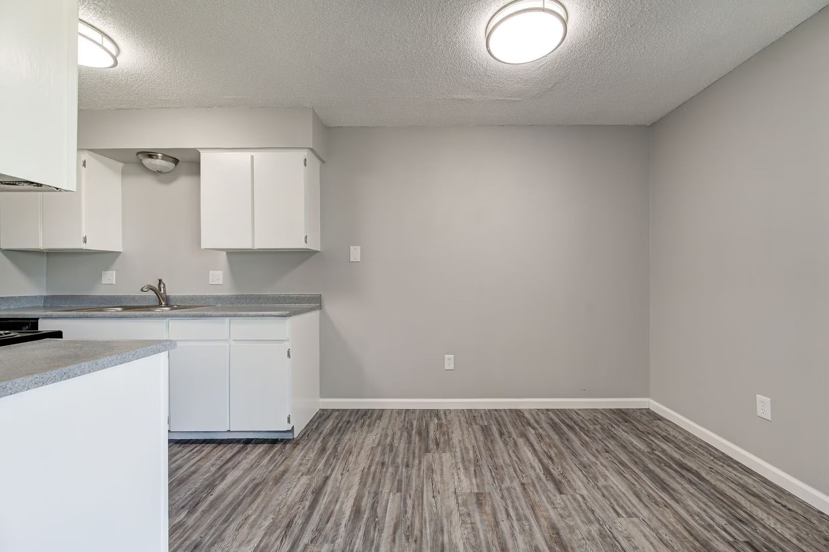 Empty kitchen with white cabinets, gray countertops and walls, and wood-look flooring.