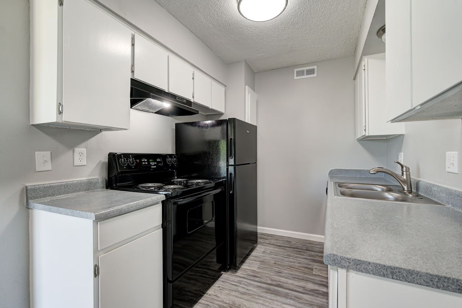A small kitchen with gray countertops, white cabinets, black appliances, and a gray-painted wall.